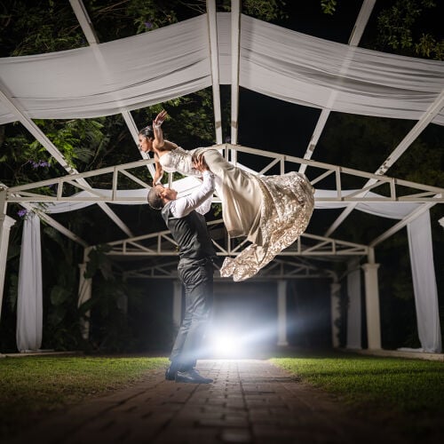 Poročna fotografija: groom lifting bride at night, couple dancing under pergola, white fabric draped overhead, nighttime wedding celebration | Heinrich Knoetze, Cape Town, Južnoafriška republika