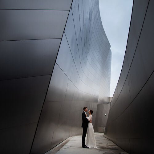 Poročna fotografija: couple kissing between buildings, modern architecture corridor, bride in white dress, groom in dark suit, overcast sky above, urban wedding portrait | Fabian Gonzales, Lima, Peru