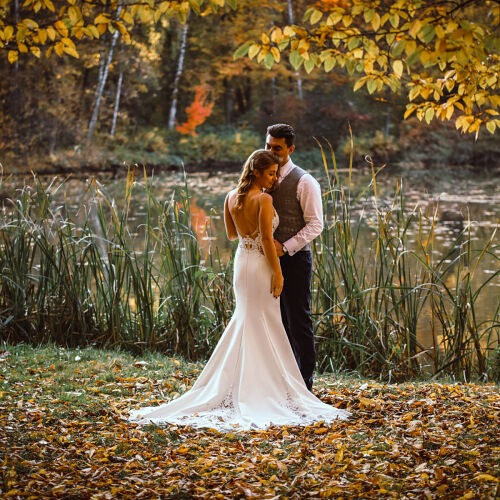 Wedding photo: Pszczyna | bride and groom by water, autumn lakeside wedding, fall foliage backdrop, golden hour light, couple among reeds, backless wedding dress | Marek Kopiec, Katowice, Poland