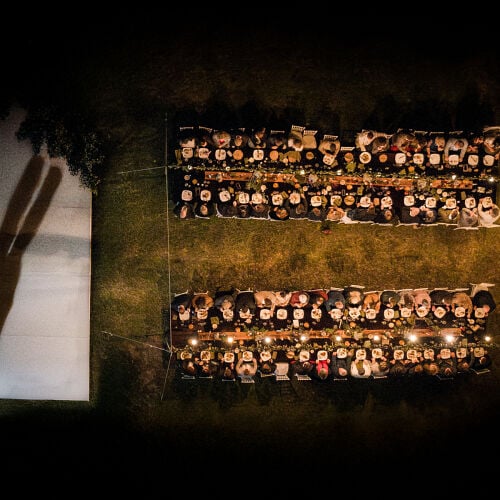 Poročna fotografija: bride in flowing veil, outdoor nighttime reception, long tables with candlelight, guests seated at dinner | Heinrich Knoetze, Cape Town, Južnoafriška republika