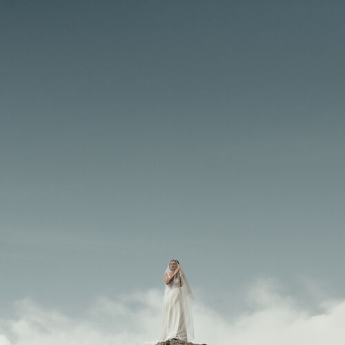 Hääkuva: bride in white veil, woman standing alone, flowing wedding dress, clear sky with clouds, minimalist outdoor setting, contemplative bride pose | Giorgi Mikeladze, Tbilisi, Georgia