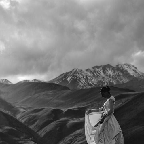 Hääkuva: bride in flowing dress, mountain landscape, dramatic cloudy sky, woman gazing at peaks, windswept fabric, monochrome alpine setting | Giorgi Mikeladze, Tbilisi, Georgia