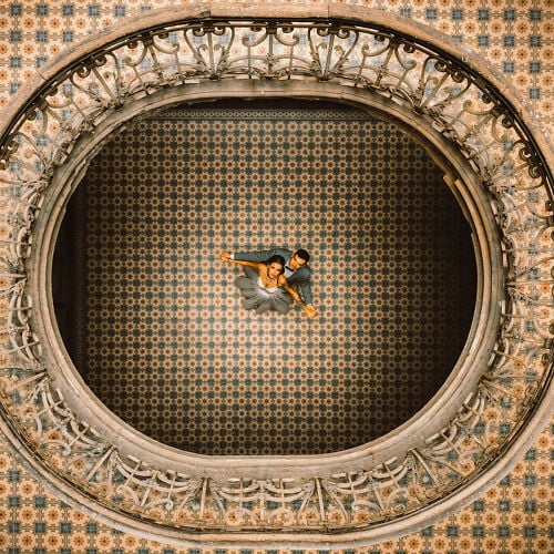Wedding photo: couple lying on ornate floor, circular architectural frame, patterned wallpaper backdrop, overhead aerial view, intimate embrace indoors | Marek Kopiec, Katowice, Poland