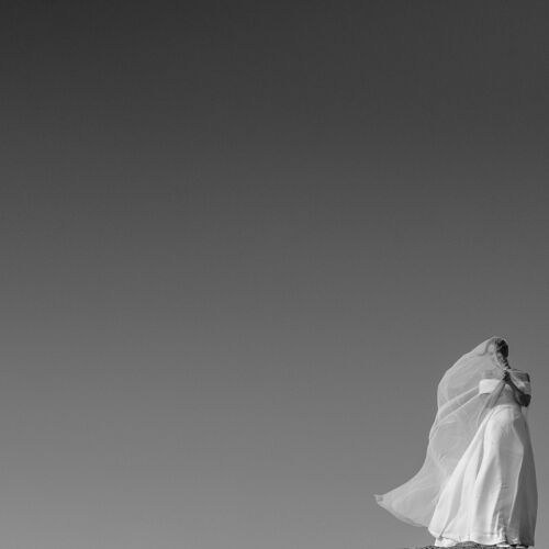 Hääkuva: bride in flowing veil, white dress billowing, clear sky backdrop, minimalist composition, solitary figure, soft natural light | Giorgi Mikeladze, Tbilisi, Georgia