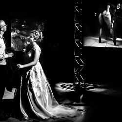 結婚式の写真: couple in dramatic lighting, bride in flowing gown, groom in suit, theatrical stage setting, black and white film, projected image on screen | Flávio Roberto, Taubaté, ブラジル