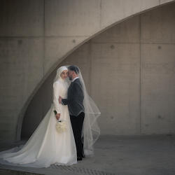 Wedding photo: bride and groom kissing, white wedding dress and veil, concrete curved wall, soft diffused light, intimate moment, modern minimalist setting | Cebi Umit , Brussels, Belgium
