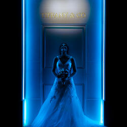 Pulmafoto: bride in wedding gown, neon blue light, luxury storefront setting, bride holding bouquet, dramatic blue neon frame, bride standing alone | Domingo García, Madrid, Hispaania