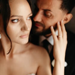 Svadobná fotografia: couple in formal attire, intimate close embrace, warm studio lighting, tender moment, dark neutral background, gentle hand touch | Andrei Hurduc, Vaslui, Rumunsko