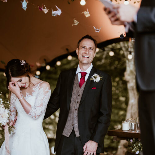 Düğün fotoğrafı: bride holding bouquet laughing, groom in grey waistcoat smiling, indoor wedding ceremony, paper crane decorations overhead | James Hatter, London, Birleşik Krallık