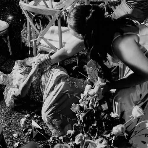 صورة زفاف: couple on grass laughing, black and white wedding, outdoor celebration, flower petals falling, guests seated nearby, playful moment on ground | John Palacio, Medellín, كولومبيا
