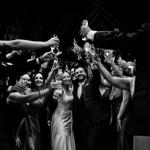Wedding photo: group toasting with champagne, black and white celebration, formal wedding reception, guests raising glasses, indoor evening party | Diego Pereira Da Silveira, Tijucas, Brazil