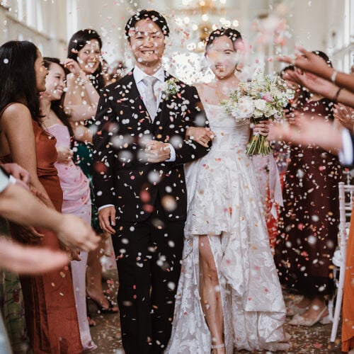 Düğün fotoğrafı: confetti toss celebration, bride and groom walking, flower crown details, white lace dress, indoor venue with chandelier, joyful wedding moment | Tom Jeavons, London, Birleşik Krallık