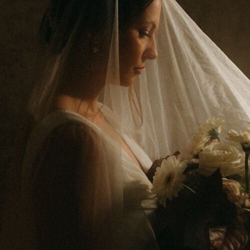 Zdjęcie ślubne: bride in white veil, holding white flowers, profile portrait, warm golden lighting, contemplative mood, soft diffused light | Sonka Skerik, Brno, Czechy