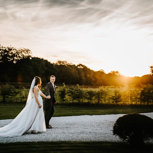 Düğün fotoğrafı: bride and groom at sunset, couple walking by water, golden hour countryside wedding, gravel path by lake, trees silhouetted at dusk | Robert Scatliffe, Lincoln, Birleşik Krallık