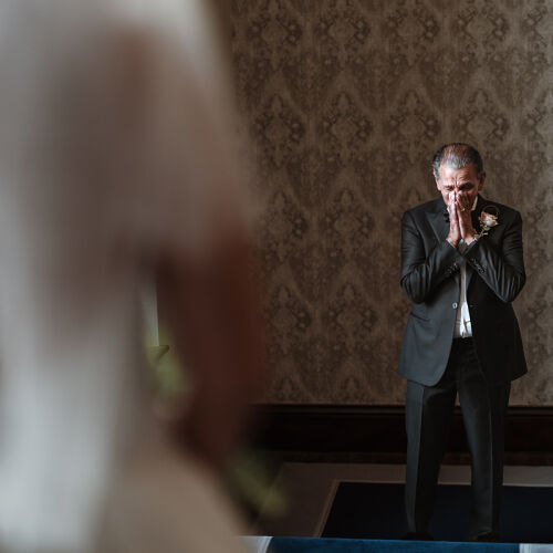Düğün fotoğrafı: groom in prayer pose, man in black suit, damask wallpaper backdrop, emotional moment indoors, soft focused foreground, formal wedding attire | James Hatter, London, Birleşik Krallık