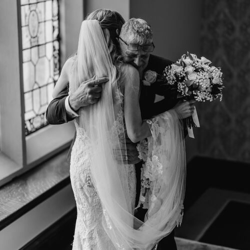 Düğün fotoğrafı: bride in lace veil, groom holding bouquet, couple embracing indoors, natural window light, black and white portrait, intimate wedding moment | James Hatter, London, Birleşik Krallık