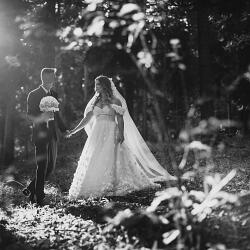 Zdjęcie ślubne: bride and groom holding hands, forest wedding ceremony, dappled sunlight through trees, bride in flowing veil, couple among flowering branches | Lukáš Molnár, Lipany, Słowacja