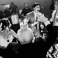 結婚式の写真: man with glass on head, formal party celebration, black and white indoor event, guests dancing and socializing, candlelit reception table | Danilo &amp; Cris Almeida, Mogi das Cruzes, ブラジル