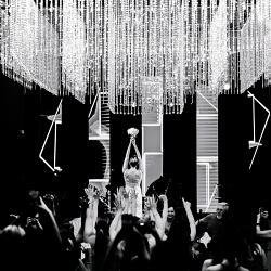 結婚式の写真: bride reaching toward chandelier, crowd with raised hands, dramatic crystal lighting, black and white ceremony, bride in white dress | Eric Corbacho, São Paulo, ブラジル