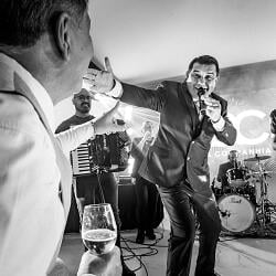 結婚式の写真: groom singing at microphone, band performing live, accordion player on stage, black and white event, man in suit speaking | Danilo &amp; Cris Almeida, Mogi das Cruzes, ブラジル